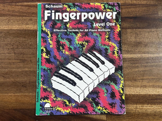 Music book titled 'Schaum Fingerpower, Level One' on a wooden surface